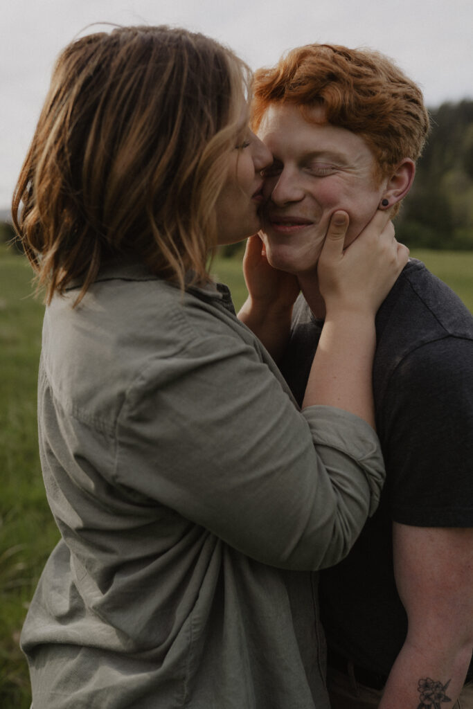 girl kisses boys cheek during engagement shoot