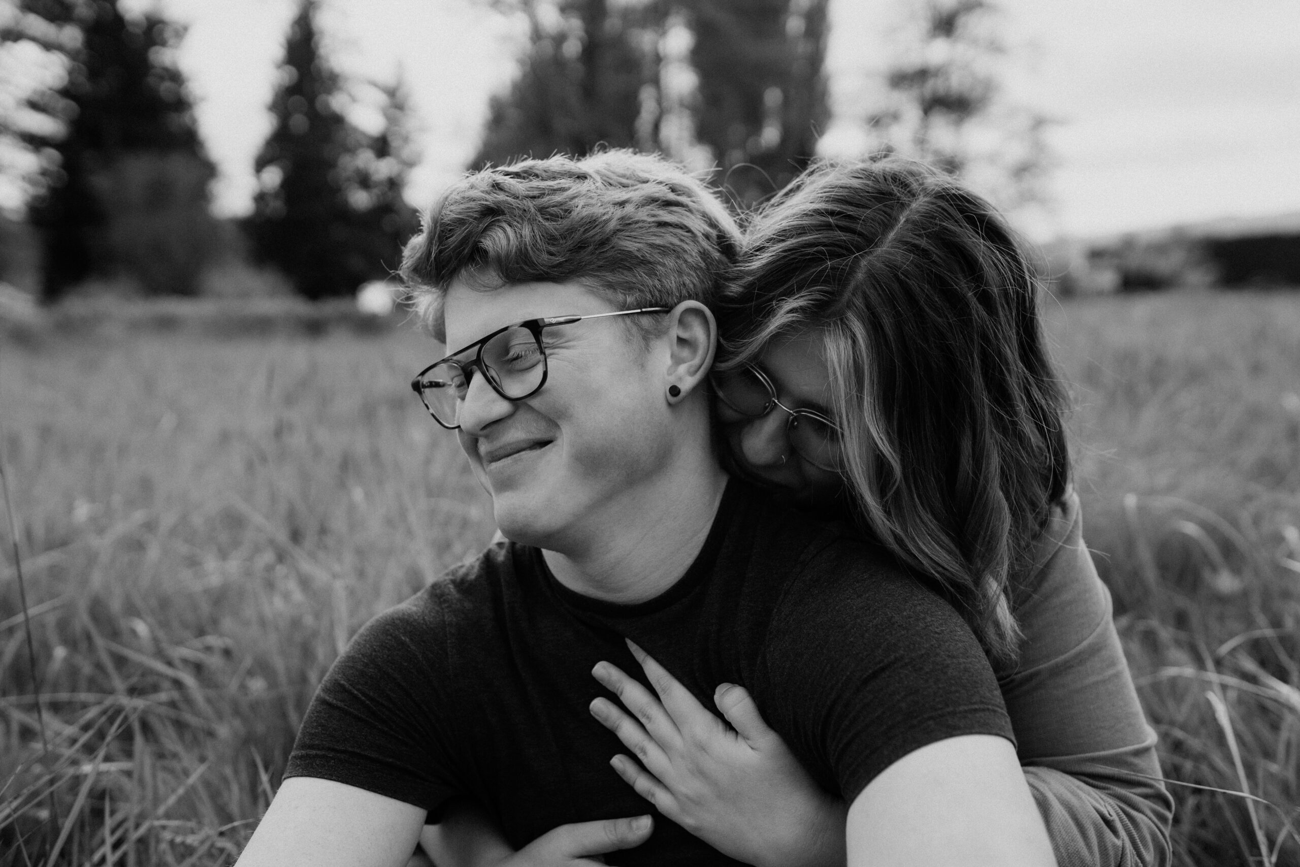 girl kisses boy on neck while sitting in a field