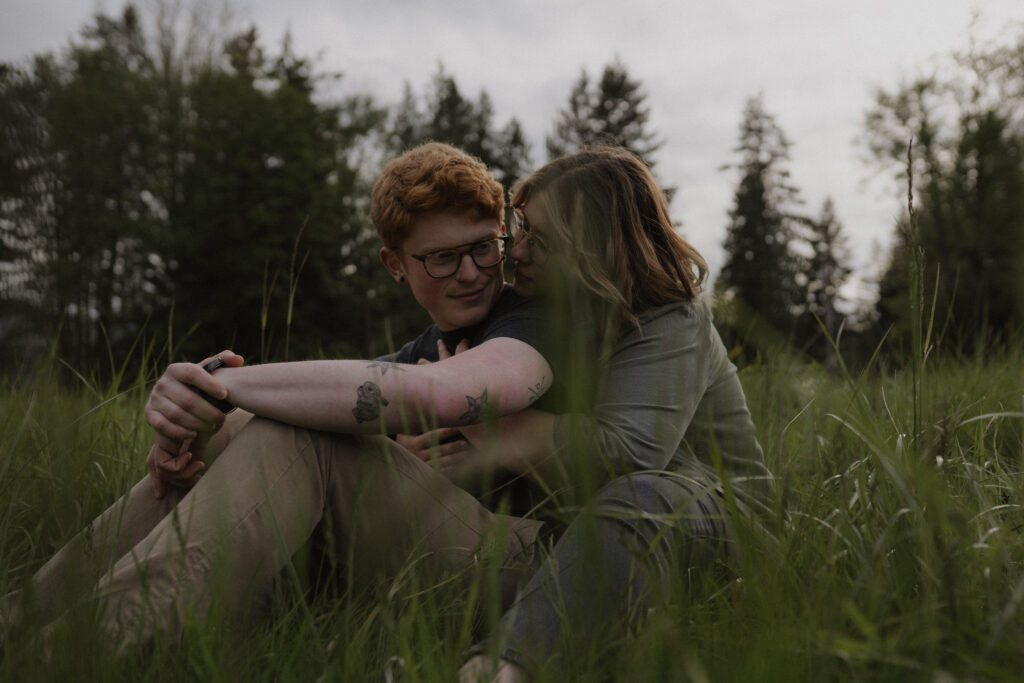 girl and boy cuddle while sitting on the ground in a field