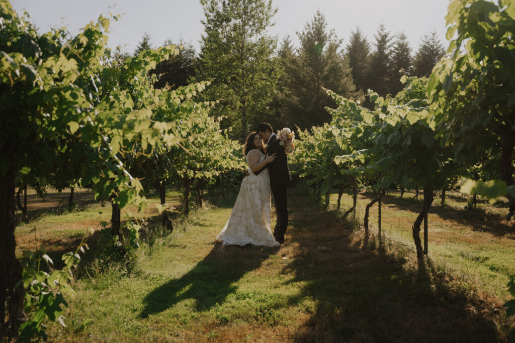 bride and groom embrace in the middle of grape vines at winery wedding