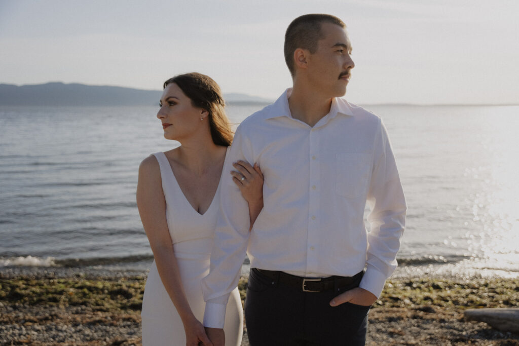 bride holds onto grooms arm as they stand in front of the ocean during Bellingham photo shoot