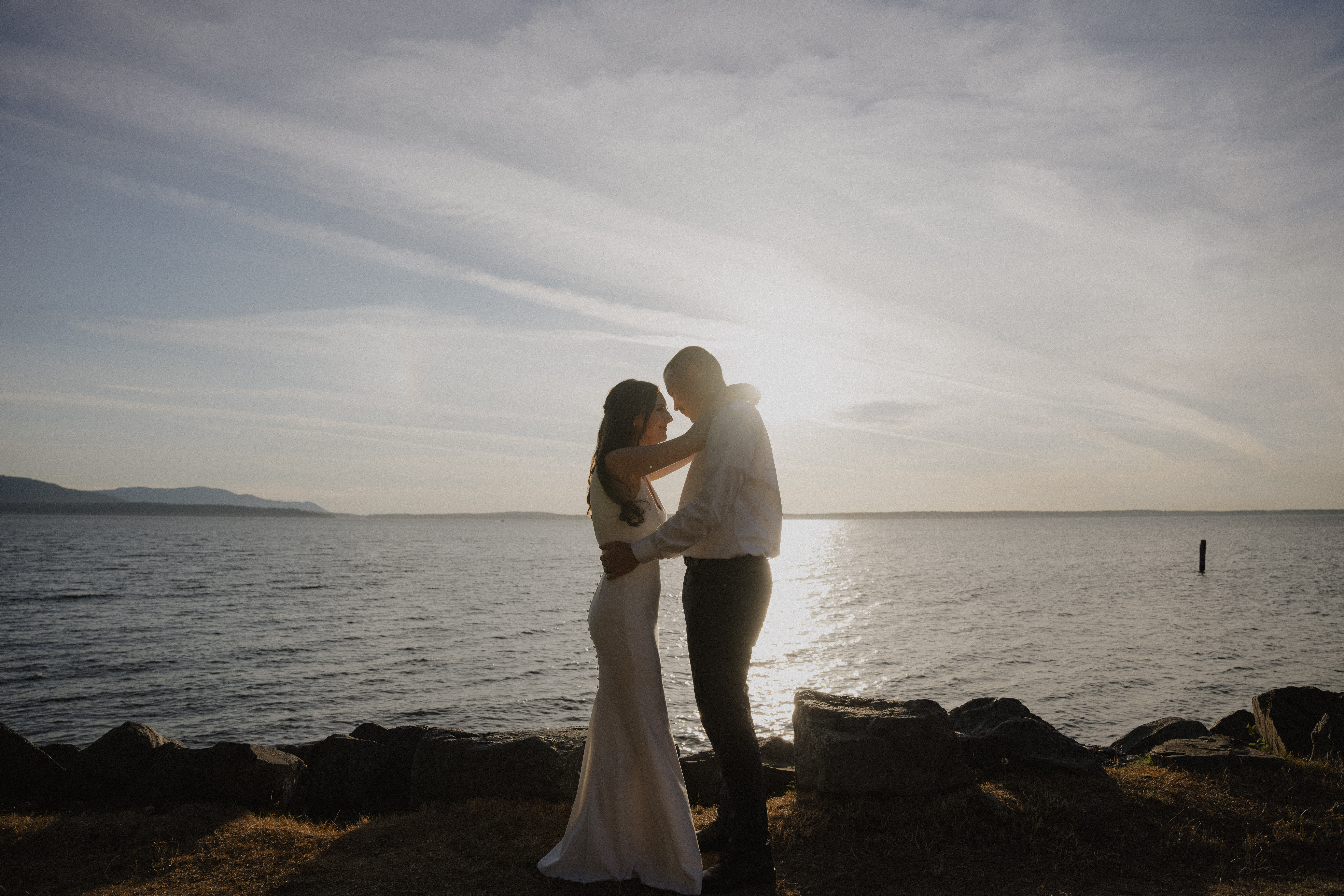 bride and groom hug in the sunlight with the ocean behind them