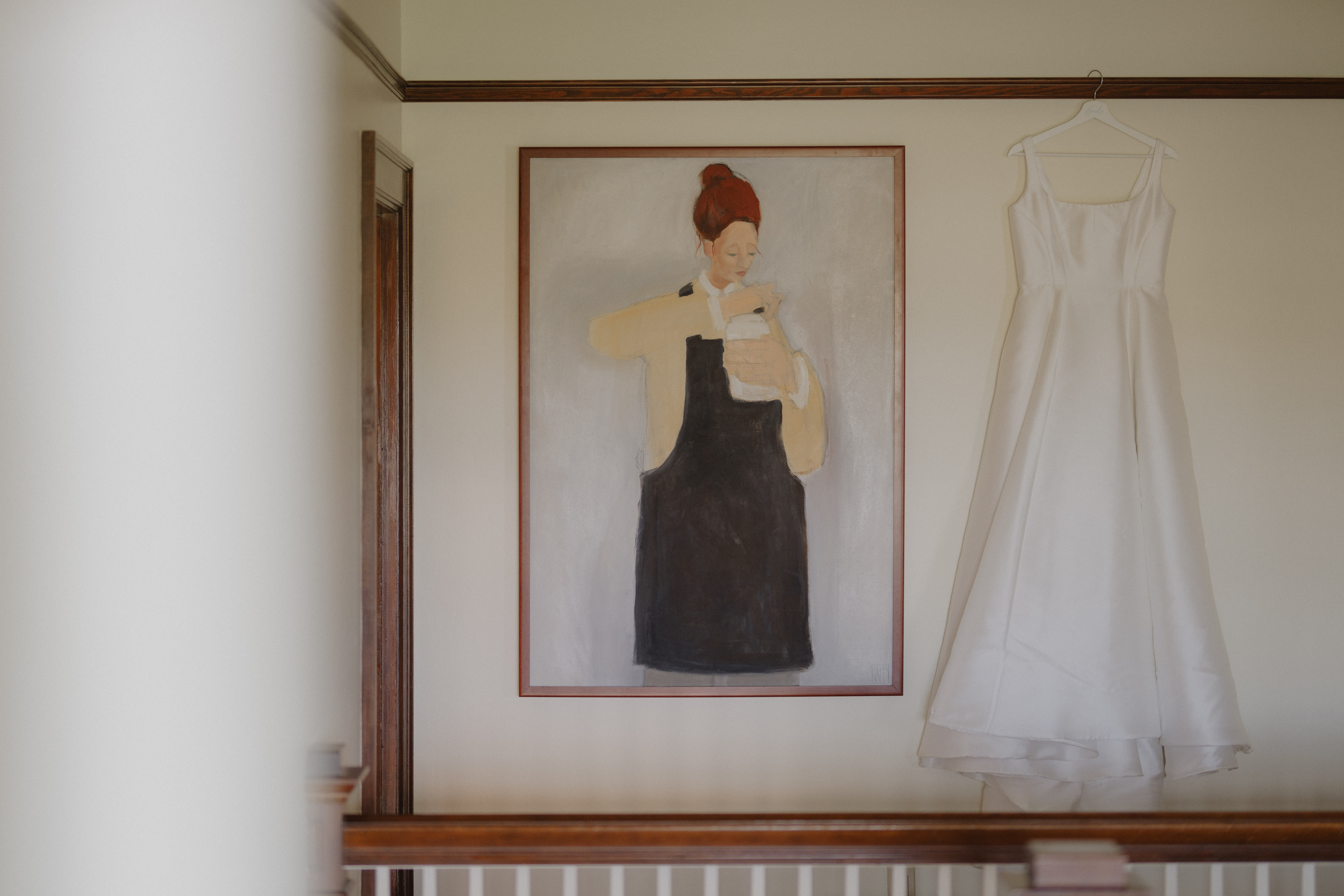 wedding dress hangs on wall next to painting at Abeja Winery wedding